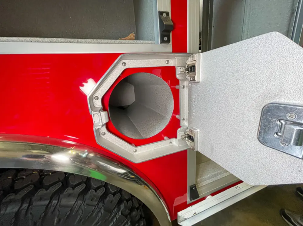 Exterior view of small fire truck showing cab, body compartments, and wheel/tire area.